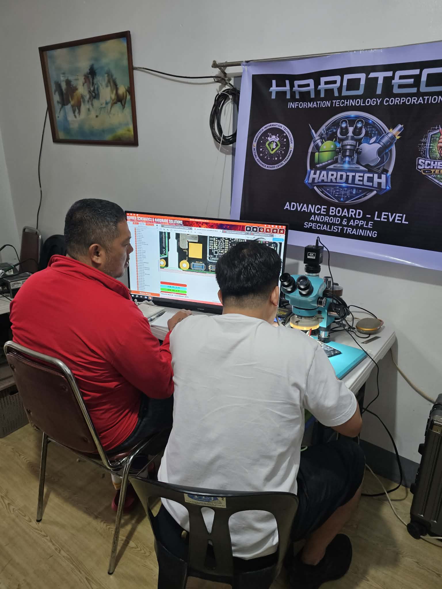 Two trainees working at a microscope station beside a HardTech training banner.