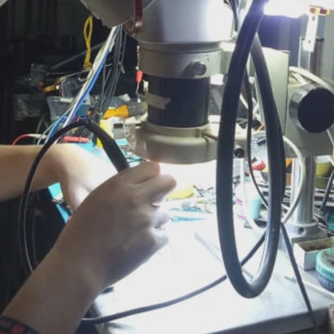Close-up of hands working under a microscope during soldering practice.
