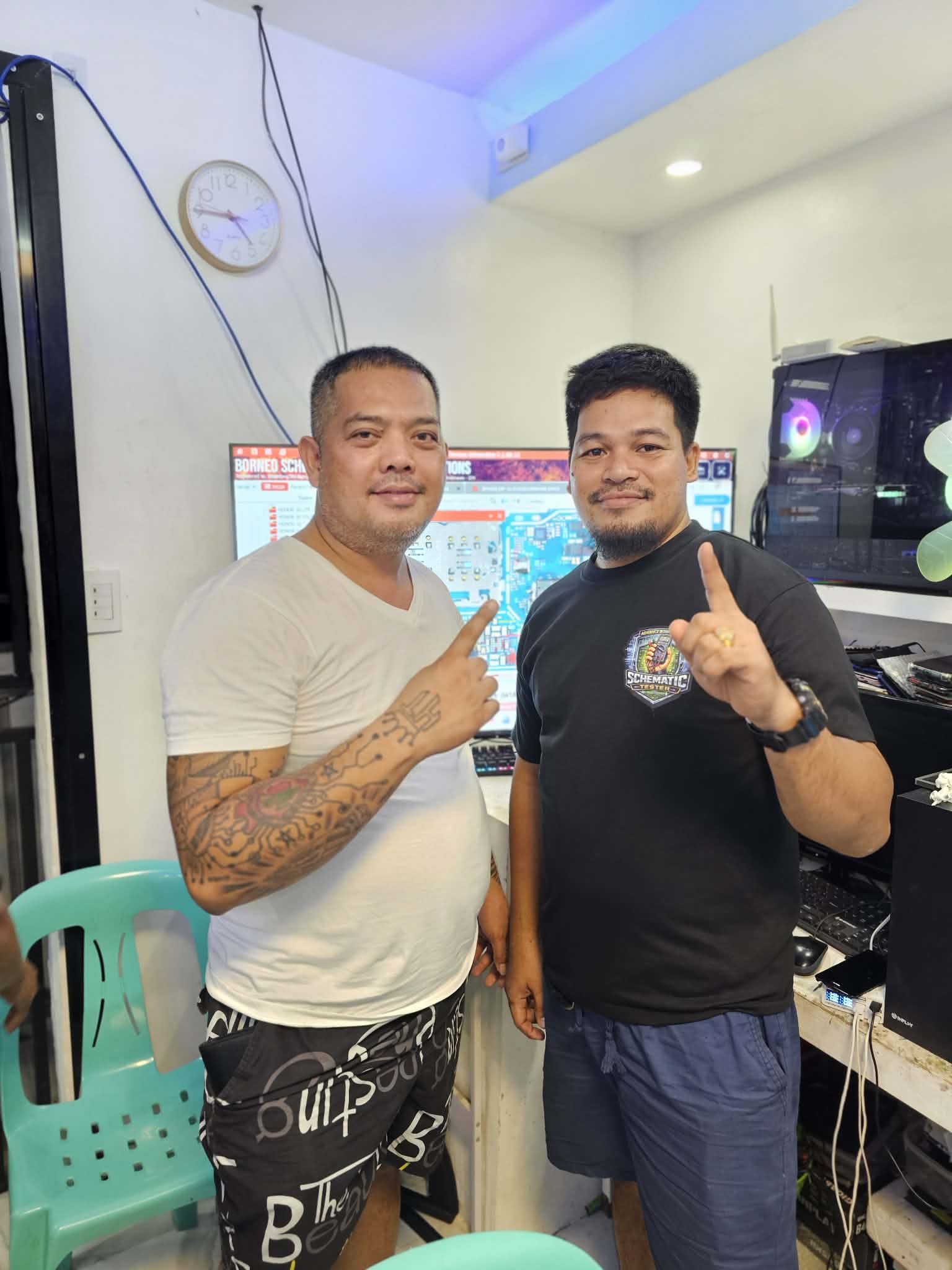Two people posing together beside a board-repair workstation.